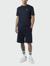 Camiseta de manga corta color azul marino con cuello redondo y un pequeño logo bordado de calavera y tibias cruzadas en blanco en el pecho.