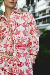 Camisa blanca con estampado de aves, edificios y motivos florales en color rojo.
