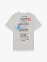 Remera de corte oversize, color blanco, con cuello redondo y mangas cortas. Presenta una estampa frontal con el texto 'ATELIER (UNVEILING VISIONS)' y tres recuadros con ilustraciones de flores.