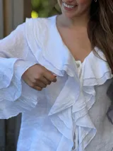 Camisa de lino azul marino con volados en cascada a lo largo del frente y en los puños de las mangas largas. Presenta un escote en V con un botón de nácar visible.