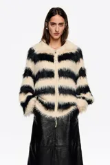 Cardigan de corte oversize confeccionado en tejido de pelo sintético con diseño de rayas horizontales en color negro y crema. Presenta cuello redondo, cierre frontal con cremallera metálica y mangas largas.