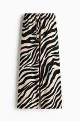 Pantalón largo de corte holgado y piernas amplias con estampado animal print de cebra. Cuenta con tiro alto, cintura elástica y cordón ajustable.