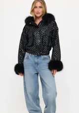 Chaqueta bomber negra con lentejuelas brillantes, cuello y puños de piel sintética. Presenta cierre frontal con botones y bolsillos delanteros con solapa.