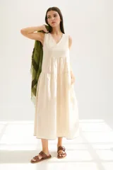 Vestido largo color beige claro, sin mangas, con escote en V y corte escalonado con frunces que le dan volumen.