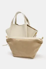 Bolso bandolera de formato city color marrón, con diseño estructurado, pespuntes decorativos, doble asa de mano y cremalleras laterales con tiradores colgantes.