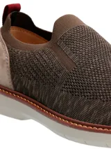 Zapato tipo slip on Hush Puppies modelo Apolo, confeccionado en tejido de poliéster color gris con refuerzo de gamuza en el talón y detalle de tirador rojo. Cuenta con suela de EVA Comfort Flex.