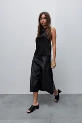 Falda midi de efecto cuero color negro, con corte evasé, tiro alto y diseño con recortes horizontales. Posee cierre lateral oculto.