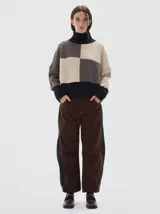 Polera de punto con diseño colorblock en tonos neutros, cuello alto, hombros caídos y mangas largas. Presenta puños, cuello y ruedo acanalados en color negro.