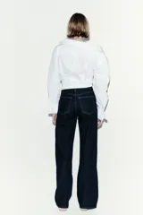 Jean de tiro alto con corte wide leg, confeccionado en denim de algodón con leve stretch. Presenta diseño clásico de cinco bolsillos, cierre frontal con botón y costuras en contraste.