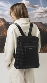 Mochila de diseño rectangular con textura símil cuero efecto cocodrilo en color tostado. Cuenta con un bolsillo frontal con cierre, compartimento principal con doble cierre, correas ajustables y manija superior. Incluye detalles metálicos y placa con logo de la marca.