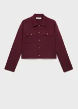 Chaqueta de punto de corte recto y diseño cropped, color bordó. Presenta cuello camisero, cierre frontal con botones dorados, mangas largas y dos bolsillos de parche con solapa en el pecho.