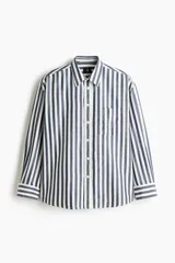Camisa de popelina de algodón con diseño de rayas verticales en azul y blanco, cuello inglés, cierre frontal de botones y un bolsillo en el pecho. Presenta mangas largas con puños abotonados y corte relaxed fit.
