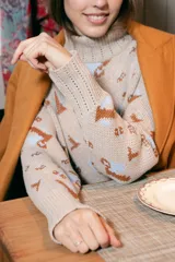 Polera de tejido de punto con cuello alto, diseño holgado y estampado jacquard con motivos geométricos y figuras en tonos beige, naranja y celeste.