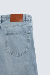 Jeans de denim de algodón en color negro con efecto lavado, corte amplio y silueta curva tipo barrel fit con pinzas en las rodillas. Presenta diseño clásico de cinco bolsillos y cierre frontal con cremallera y botón metálico.