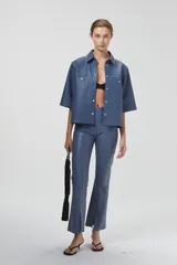 Sobre camisa azul de cuero ovino, corte boxy, mangas cortas, cuello clásico, botones a presión plateados y bolsillos delanteros.