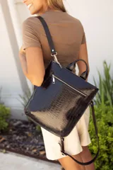 Mochila negra de cuero con textura tipo cocodrilo, doble asa corta superior y correa larga regulable para usar al hombro o como mochila. Cierre superior con cremallera y bolsillo frontal con cremallera.