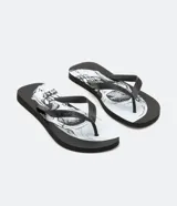 Chinelas negras con base blanca y estampado de calaveras en blanco y negro. Las tiras son negras con diseño geométrico en relieve.