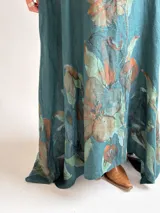 Vestido largo verde petróleo con estampado floral grande en tonos marrones y ocres, de corte amplio, mangas tres cuartos y escote en V.