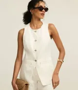 Chaleco largo color crudo confeccionado en sarga de algodón, con cuello redondo, cierre abotonado, bolsillos delanteros y cintura ajustada.