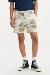 Bermuda de corte clásico con estampado tropical de palmeras y paisajes en tonos tierra sobre fondo beige. Cuenta con cierre de botón y cremallera, bolsillos laterales y bolsillos traseros.