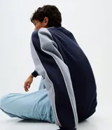 Buzo de corte boxy con cuello redondo y mangas largas raglán. Presenta un diseño bicolor en azul marino y gris, con detalles de piping en contraste y lettering bordado en el pecho.
