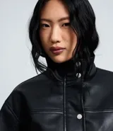 Campera bomber de poliuretano con cuello alto estructurado, cierre frontal con botones de presión, bolsillos utilitarios delanteros y ruedo con elástico para un ajuste cómodo.