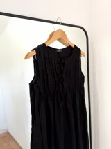 Vestido negro sin mangas, con escote redondo y detalle de pliegues verticales en el frente, con lazo ajustable en el escote.
