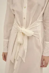 Vestido camisero largo color crema, de algodón, con cuello clásico, mangas largas con puños abotonados, cierre frontal con botones nacarados y lazo para atar en la cintura.