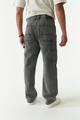 Jean estilo carpenter de corte relajado, recto y amplio, con diseño de cinco bolsillos y costuras reforzadas características del modelo. Presenta un acabado lavado en tono gris oscuro.