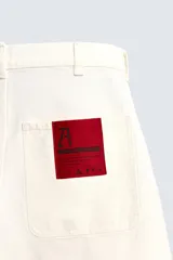 Bermuda de denim color crudo o blanco roto, de corte ancho (baggy fit) y largo hasta la rodilla. Presenta cinco bolsillos, bordado a tono en el frente y un parche con logo en la parte trasera.