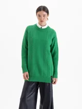 Sweater de tejido de punto con diseño de trenzas verticales y textura en relieve. Presenta cuello redondo, mangas largas y un corte holgado con terminaciones en rib. Incluye una etiqueta decorativa en el ruedo.