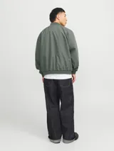 Campera bomber verde militar, liviana, de manga larga con cuello baseball y corte cómodo. Tiene cierre frontal de cremallera, bolsillos delanteros y puños de canalé.