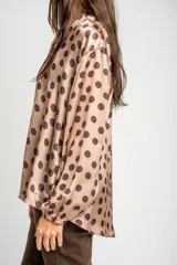 Camisa oversize de poliéster color rosa con estampado de lunares marrón oscuro, cuello camisero, cierre frontal de botones y mangas largas con puños elásticos.