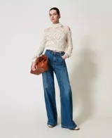 Sweater color crema de punto calado con motivo de rombos, cuello alto con volados y hombros descubiertos. Tiene mangas largas holgadas, ribetes acanalados, bajos festoneados y corte holgado.