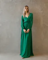 Vestido largo de satén color verde esmeralda, con escote cruzado, mangas largas amplias con puños elásticos y cintura marcada con lazo ajustable.