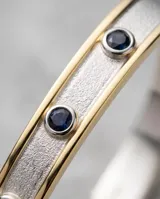 Esclava rígida de plata 925 con aplique de lámina de oro 18k, decorada con tres incrustaciones circulares de piedras azules.
