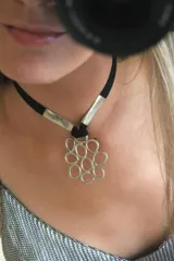 Gargantilla con cordón de cuero negro, apliques metálicos plateados y dije con forma de flor geométrica plateada.