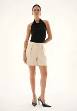 Bermuda de vestir color beige, de corte sastrero con pinzas frontales, bolsillos laterales y cierre de botón y cremallera.