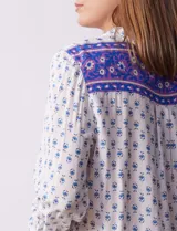 Camisa blanca con estampado floral en azul, de manga larga y cuello con solapa.