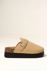 Zueco de plataforma color beige, con capellada de gamuza sintética, detalle de hebilla metálica lateral y suela de goma negra con detalle de corcho en el talón.