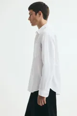 Camisa H&M de corte relajado, confeccionada en tejido liviano de mezcla de lino y algodón color blanco. Presenta cuello inglés, cierre frontal de botones, manga larga con puños ajustables y bolsillo aplicado en el pecho.