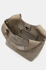 Bolso mini shopper de piel color gris topo, con doble asa de mano y asa bandolera extraíble. Cuenta con bolsillo interior con cremallera y cierre mediante botón imantado.