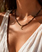 Collar corto de cristalitos facetados en tonos marrones oscuros, con cuentas metálicas doradas y un dije colgante en forma de luna creciente de acero dorado.