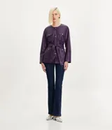 Campera alargada marca Cortelle confeccionada en poliuretano con textura que imita el cuero. Presenta cuello redondo, cierre frontal con botones metálicos, cuatro bolsillos delanteros con solapa y botones, y un lazo ajustable en la cintura.