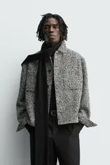 Sobrecamisa de corte relajado con textura de tejido estructurado en color gris y negro. Presenta cuello clásico, cierre frontal con botones, mangas largas con puños abotonados y bolsillos de plastrón en el pecho.