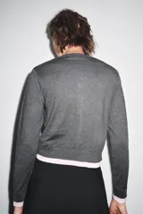 Chaqueta de punto gris de manga larga, cuello redondo y cierre frontal con botones oscuros. Presenta ribetes y detalles en color azul eléctrico en el frente, puños y ruedo.