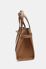 Bolso tipo mini shopper de cuero sintético color marrón caramelo, con costuras blancas visibles. Posee asas de mano y una correa bandolera ancha de tela color beige. El frente tiene un detalle de tira con hebilla metálica dorada.