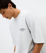 Remera gris melange de corte relaxed, con cuello redondo y mangas cortas. Presenta un diseño gráfico en la espalda con estampado y textura en alto relieve embossed que incluye la frase "Beyond Limits: Keep Going" y el texto "The Urban Supply Co. of N.Y.C.".