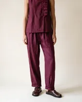 Pantalón de lino color bordó, con silueta relajada, cintura elastizada con lazo de ajuste, bolsillos laterales y detalle de pliegues con ruedo desflecado en los tobillos.