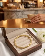 Pulsera tipo esclava rígida de acero con baño de oro, con diseño de eslabones texturizados y esferas lisas intercaladas.